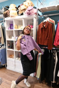 A young girl holding up a purple cropped jacket from a charity shop