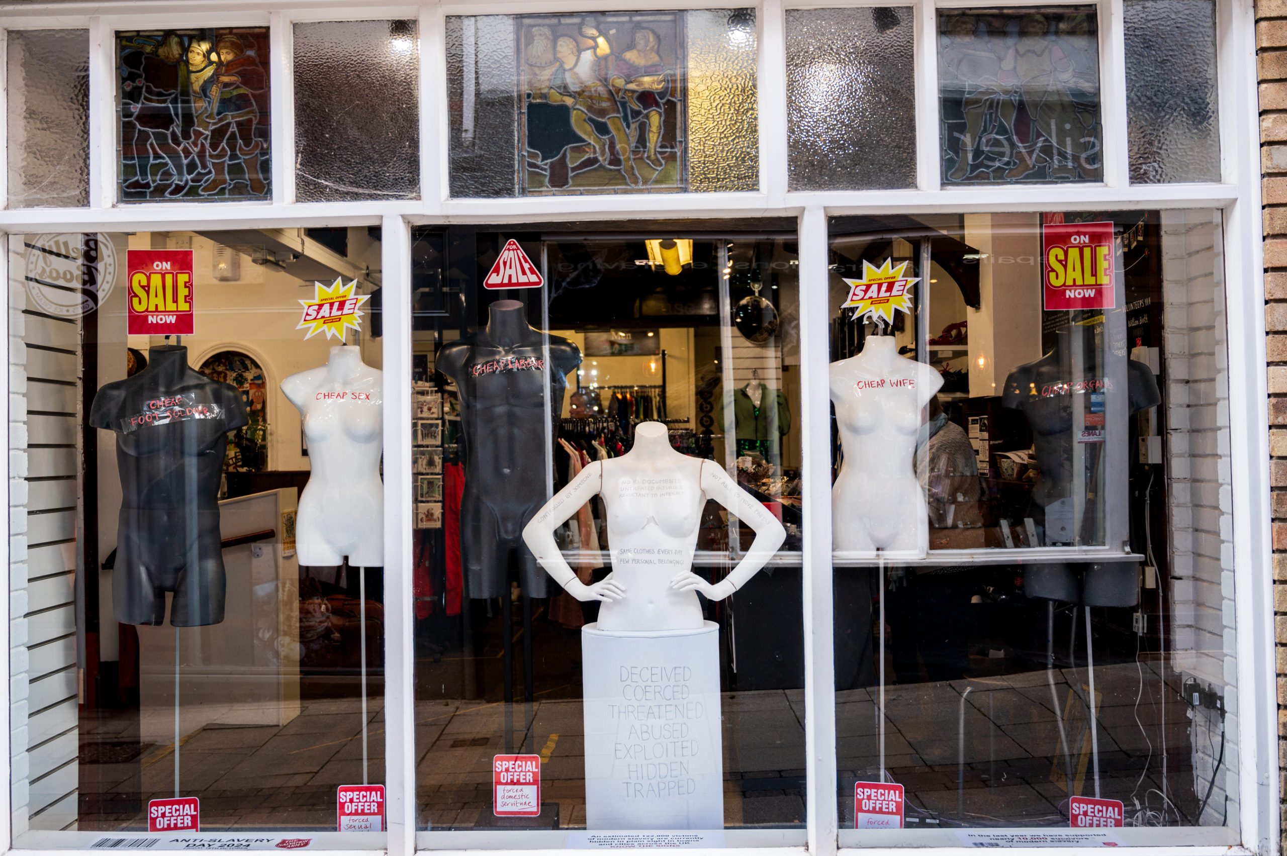 window display showing 5 naked mannequins with written messages on them. SALE signs at the top of the mannequins and SPECIAL OFFER signs at the bottom. 