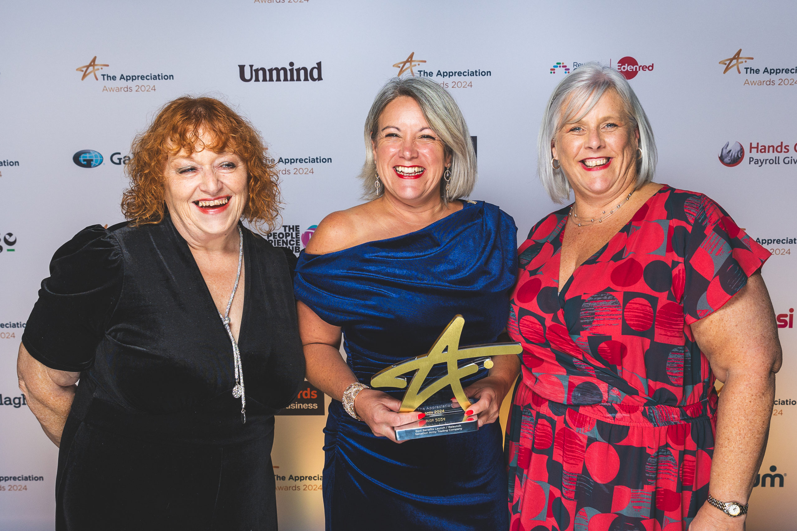 three women posing, the middle lady is holding an award that looks like the letter A (also like a star).