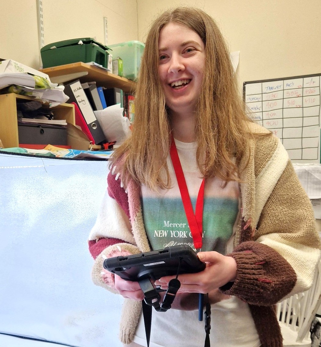 Volunteer with red volunteer lanyard, holding ipad, smiles at camera