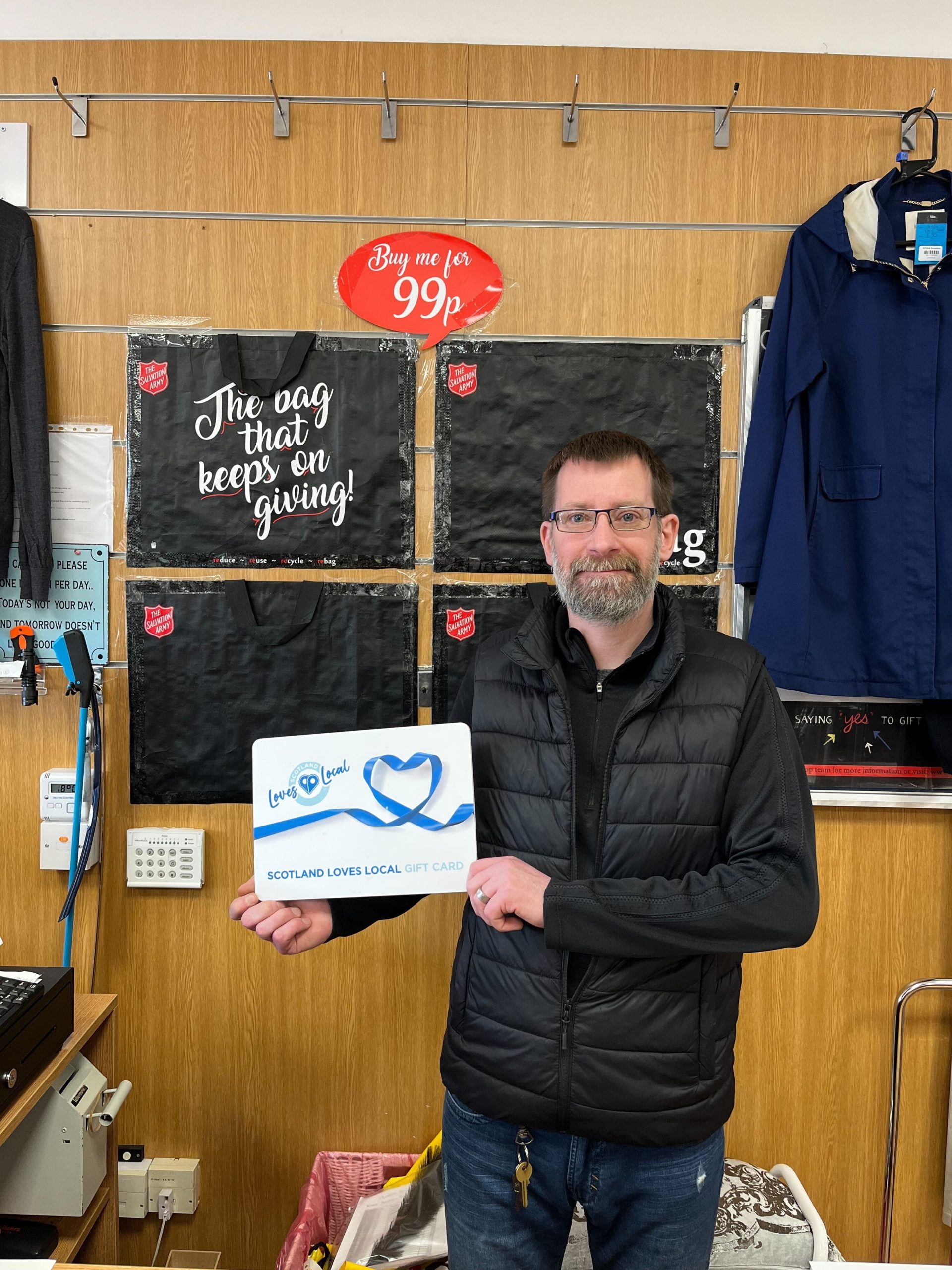 Salvation Army colleague standing behind the till, holding a Scotland Loves Local gift card.