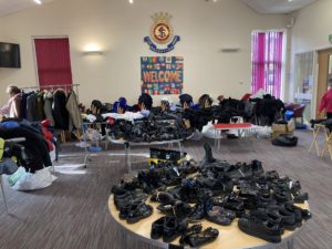 Large Salvation Army hall has tables with lots of uniform items on display, in the foreground is a table filled with black shoes